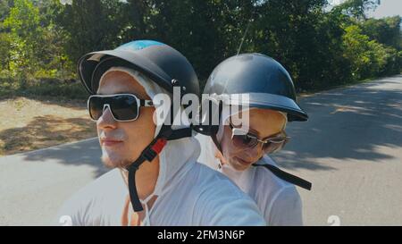 Zwei kaukasische Touristen Mann fahren auf roten Roller. Machen Sie es Selfie. Ich liebe ein Paar auf einem Motorrad in weißen Kleidern, um auf einem Waldweg zu fahren. Stockfoto