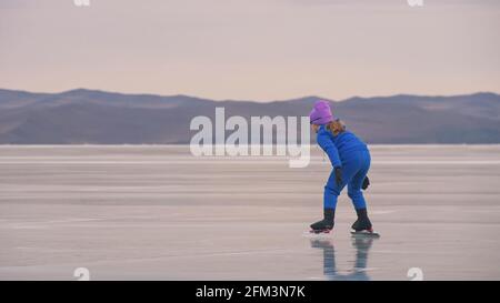 Das Kind trainiert auf Eisschnelllauf. Das Mädchen Schlittschuhe im Winter in Sportbekleidung, Sportbrille, Anzug. Zeitlupe im Freien. Stockfoto