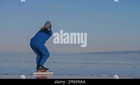 Das Kind trainiert auf Eisschnelllauf. Das Mädchen Schlittschuhe im Winter in Sportbekleidung, Sportbrille, Anzug. Zeitlupe im Freien. Stockfoto