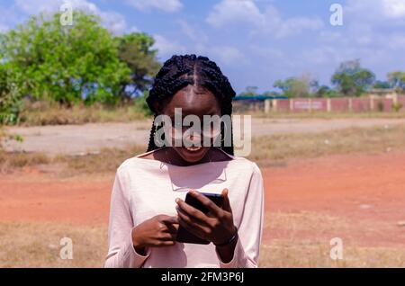 Junge afrikanische Frau, die ihr Telefon ansieht, nachdem sie Gutes empfangen hat nachrichten Stockfoto
