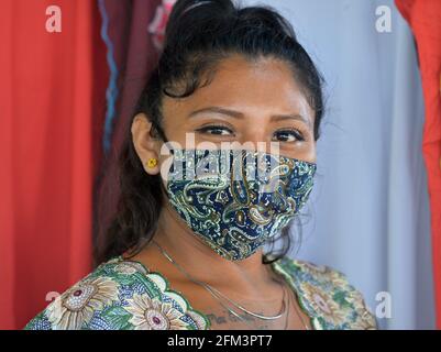 Braunäugige mexikanische Verkäufin mit schönem Augen-Make-up trägt während der globalen Coronavirus-Pandemie eine nicht-medizinische Gesichtsmaske aus folklorischem Gewebe. Stockfoto