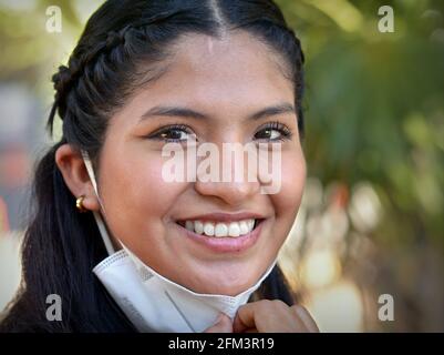 Lächelnd glücklich optimistisch Mexikanisch junge Brünette Latina Frau mit schönen braunen Augen zieht ihre KN95 Gesichtsmaske nach unten und schaut auf den Betrachter. Stockfoto