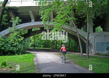 Fahrradfahrer peddeln entlang des Minnehaha Parkway Regional Trail, der unter dem Bogen der Nicollet Avenue Bridge verläuft. Minneapolis Minnesota, USA Stockfoto