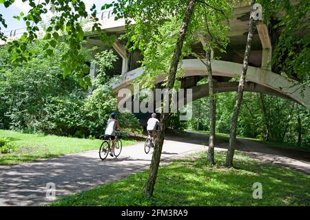 Fahrradfahrer, die entlang des Minnehaha Parkway Regional Trail fahren und unter einem der Bögen der Nicollet Avenue Bridge vorbeifahren. Minneapolis Minnesota, USA Stockfoto