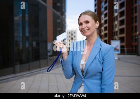 Business stilvolle Frau in einer blauen Jacke hält ein Abzeichen In der Hand vor dem Hintergrund eines Bürogebäudes Stockfoto