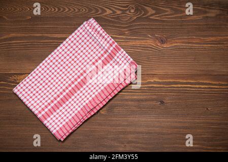 Karierte Stoffserviette oder Küchentuch auf brauner Holzoberfläche. Tischdecke auf Tischplatte, Draufsicht. Stockfoto
