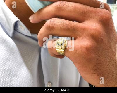 Alicante, Spanien - April, 2021: Großer goldener Versace-Ring auf der Hand eines jungen Mannes mit Gesichtsmaske Stockfoto