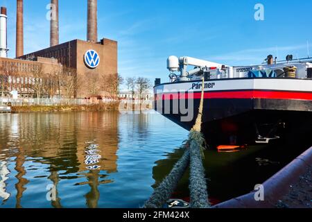 Das Frachtschiff ist mit einem dicken Seil an den Pier gebunden, während sich das Kraft-Wärme-Kopplungs-Kraftwerk von VW im Wasser des Kanals in Wolfsburg widerspiegelt Stockfoto