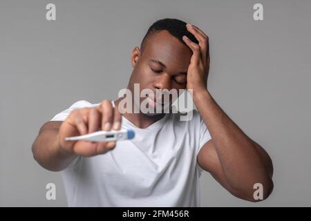 Afro american zeigt Thermometer, das Hand an Kopf berührt Stockfoto