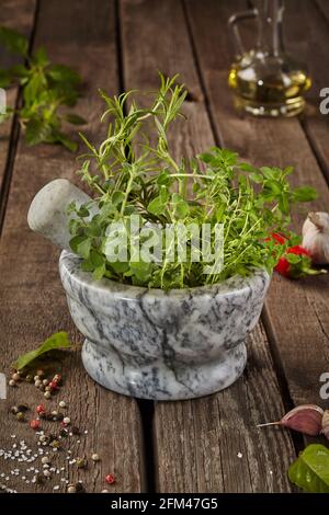 Duftende Kräuter in Mörtel auf Holztisch mit Gewürzen und Öl Stockfoto
