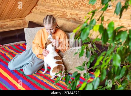 Ein Mädchen umarmt und küsst einen kleinen Hund in einem gemütlichen Interieur eines Landhauses. Stockfoto