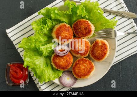 Saftig lecker überzogen mit Paniermehl und gebratenen Hähnchenschnitzel auf weißem Teller mit Gewürzen und Cetchup auf dunklem Hintergrund, Blick von oben. Stockfoto