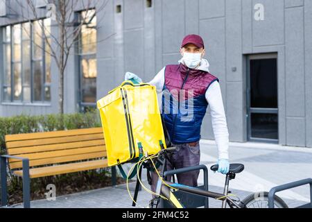 Ein junger Kurier liefert Essen mit einem gelben Thermalrucksack und fährt mit dem Fahrrad in der Stadt. Konzept für den Lieferservice von Lebensmitteln Stockfoto