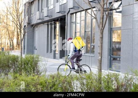 Ein junger Kurier liefert Essen mit einem gelben Thermalrucksack und fährt mit dem Fahrrad in der Stadt. Konzept für den Lieferservice von Lebensmitteln Stockfoto