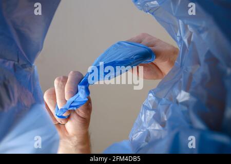 Eine Hand schmeißt blaue medizinische Handschuhe in einen Mülleimer.man entfernt Schutzhandschuhe aus der Hand über den Müllkorb. Ansicht von unten. In Innenräumen. Stockfoto