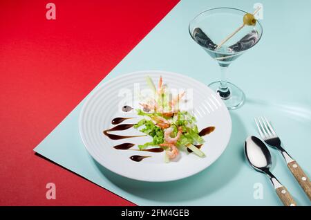 Moderne Küche: Seafood-Salat mit Grüns und Teriyaki-Sauce mit Cocktail-Dekor aus grüner Olive auf rotem und minzfarbenem Hintergrund, Kopierbereich. Stockfoto