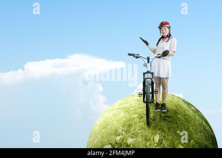 Asiatische Frau mit einem Fahrradhelm, der neben ihrem Fahrrad auf dem Wiesenfeld steht. Weltfahrradtag Stockfoto