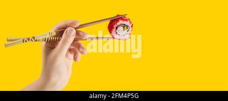 Frauenhänden halten Sushi-Rollen mit Stöcken. Gelber Hintergrund. Kreatives Konzept Stockfoto