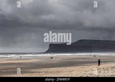 Menschen, die am Strand spazieren, während Sturmwolken über Saltburn-by-the-Sea und Huntcliff, North Yorkshire, Großbritannien, Rollen Stockfoto