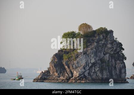 Panoramablick auf den Sonnenuntergang über dem glitzernden Wasser, den Felsformationen, den blauen Bergen und den schwimmenden Booten in der Halong-Bucht in Vietnam Stockfoto