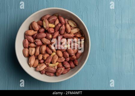 Eine Schüssel voller geschälter Erdnüsse auf blauem Hintergrund Stockfoto