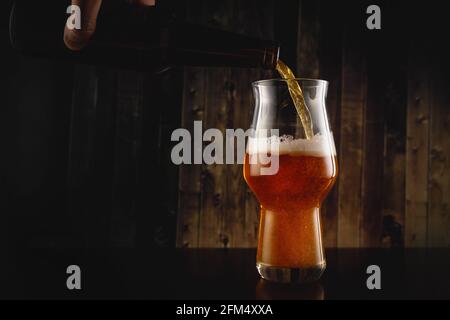Bier aus der Flasche auf Holzgrund in das Glas gießen. Stockfoto