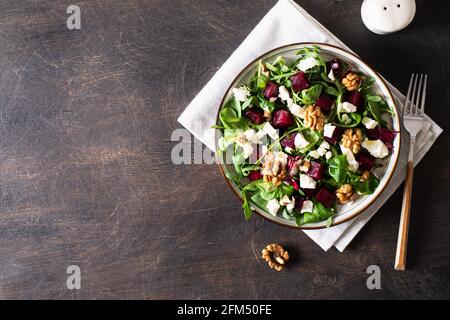 Rüben- oder Rote Beete-Salat mit frischer Rucola, Weichkäse und Walnüssen auf dem Teller, Dressing und Gewürzen auf dunklem Holzhintergrund, Kopierraum, Draufsicht/ Stockfoto