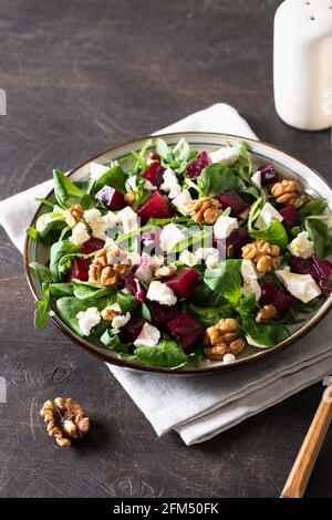 Rüben- oder Rote Beete-Salat mit frischer Rucola, Weichkäse und Walnüssen auf dem Teller, Dressing und Gewürzen auf dunklem Holzhintergrund, Kopierraum, Draufsicht/ Stockfoto