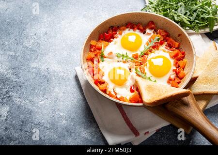 Leckere und gesunde Shakshuka in einer Bratpfanne. Eier pochiert in würziger Tomatensauce. Spiegeleier mit Toast, Rucola Stockfoto