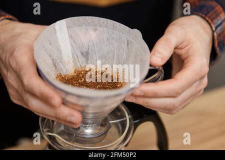 Männliche Hände gießen gemahlenen Kaffee in den Filter. Stockfoto