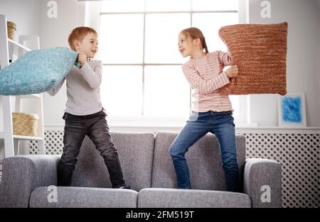 Niedliche Kinder kämpfen mit Kissen auf dem Sofa Stockfoto