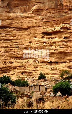 Ein Dorf in Dogon am Fuße der Falaise de Bandiagara. Die spitzen Strohdächer gehören zu den Dorfvorratskammern. In der Felswand sieht man die Stockfoto