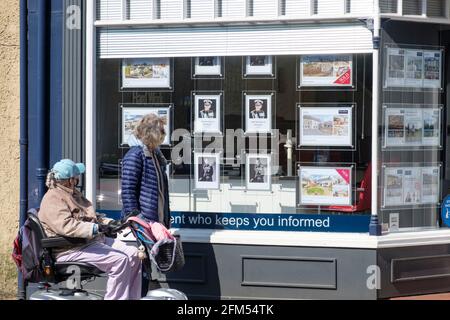 Zwei Personen sehen sich Bilder des verstorbenen Duke of Edinburgh Prince Phillip in einem Tetbury Immobilienmakler-Fenster an. Stockfoto