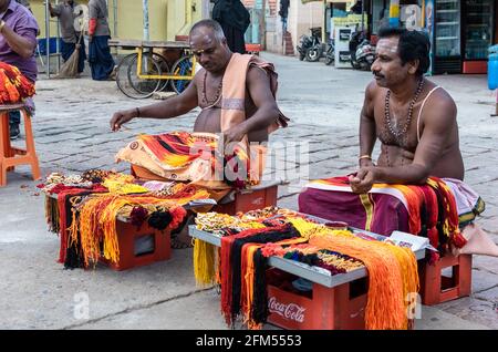 Mysuru, Karnataka, Indien - 2019. Januar: Indische Männer in traditioneller Kleidung verkaufen bunte Bänder für hinduistische Rituale im alten Tempel in Chamundi Stockfoto