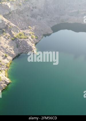 Felsige Ufer des Radon Lake an einem sonnigen Sommermorgen. Luftaufnahme eines alten überfluteten Granitsteinbruchs. Ein malerischer Teich. Stockfoto