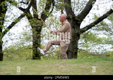 Ein älterer asiatischer Amerikaner, wahrscheinlich Chinese, macht Tai-Chi-Übungen mit einem langen Stock. Auf einem Hügel in einem Park in Queens, New York City. Stockfoto