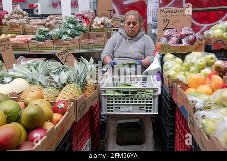 Eine Frau, die einen Obst- und Gemüsestand unter dem el in Corona betreibt, streift ein Kaktusblatt. In New York City. Stockfoto