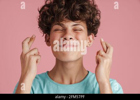 Lächelnder junger Mann mit gekreuzten Fingern auf rosa Hintergrund. Stockfoto
