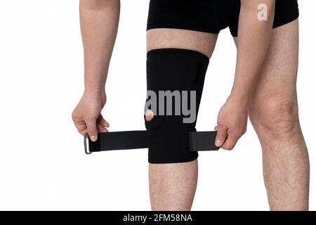 Orthese am männlichen Bein. Ein Mann fixiert eine schwarze Orthese auf seinem Bein. Isoliert auf weißem Hintergrund. Stockfoto