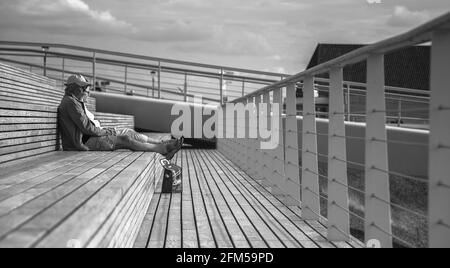 Ein älteres Paar, das sich auf einer Terrasse am Yachthafen entspannen und auf die man blicken kann Im Sommer auf der anderen Seite des Meeres trinken Stockfoto