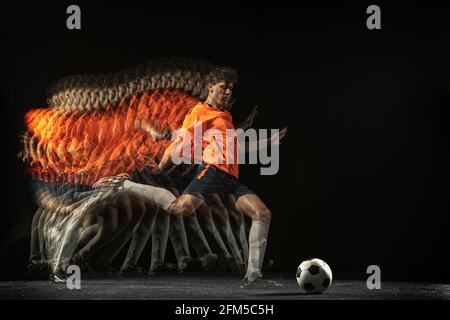 Ein kaukasischer Fußballspieler in Bewegung und Action in gemischtem Licht auf dunklem Hintergrund. Stockfoto