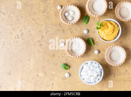 Leere Shortbread-Tartlets, Zitronenkurz, Mini-Bagues und Minze auf betontem Hintergrund. Verarbeiten Sie das Dessert. Draufsicht. Selektiver Fokus. Stockfoto