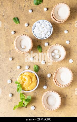 Leere Shortbread-Tartlets, Zitronenkurz, Mini-Bagues und Minze auf betontem Hintergrund. Verarbeiten Sie das Dessert. Draufsicht. Selektiver Fokus. Stockfoto