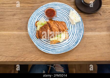 Croissant mit gegrilltem Käse und Salat auf dem Teller, Holztisch im Café, Café. Leckeres Sandwich. Frühstück oder Mittagessen. Stockfoto