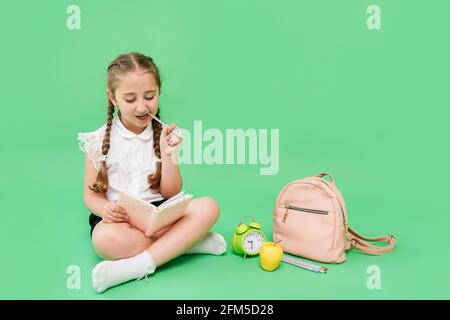 Nettes Schulmädchen in Uniform sitzt auf grünem Hintergrund und reeding Buch, kopieren Raum Stockfoto