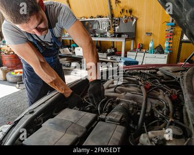 Ein Mechaniker repariert den Motor eines Autos unter der Motorhaube in einer Werkstatt-Garage. Stockfoto