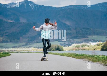 Nettes Mädchen Skateboarding auf dem Longboard auf der Asphaltstraße mit einer Berglandschaft Hintergrund. Sie schob sich anmutig ab und verlangsamte das Reiten. Alles gute Stockfoto