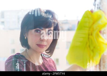 Frau, die zu Hause Fenster wascht, wischt das Glas mit einem Lappen. Stockfoto