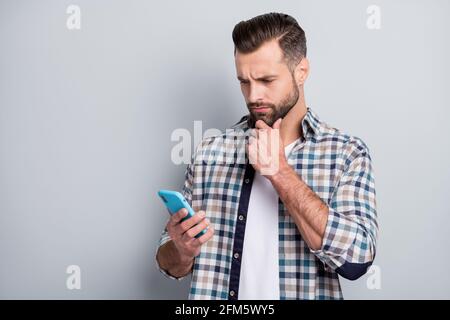 Foto von jungen schönen schweren thougtfuk gesinnten Mann denken halten Mobiltelefon auf grauem Hintergrund isoliert Stockfoto