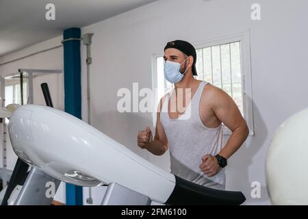 Mann, der auf einem Laufband läuft und eine Maske trägt. Covid19. Gesundheits- und Sicherheitskonzept. Stockfoto